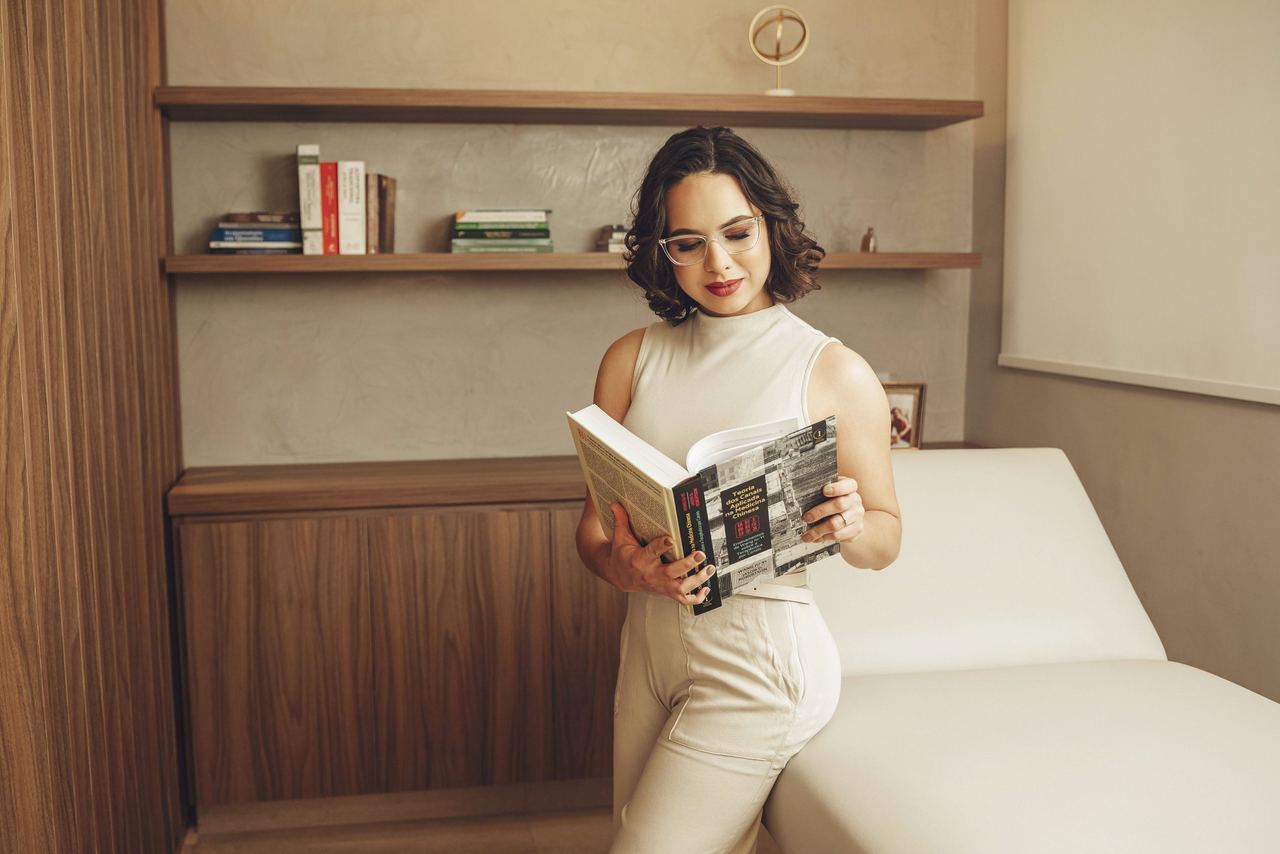 Dra. Thaís lendo um livro, apoiada na maca do consultório.